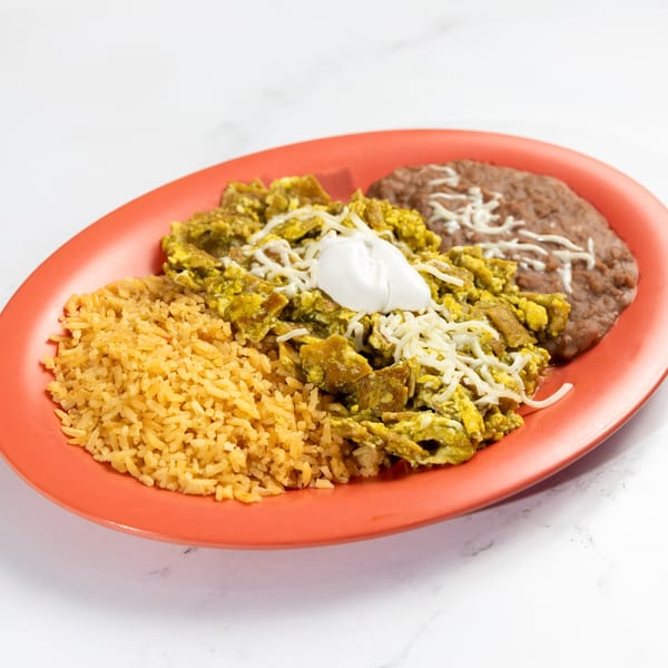 De Pasada's chilaquiles with green sauce, rice, and refried beans on an orange plate.