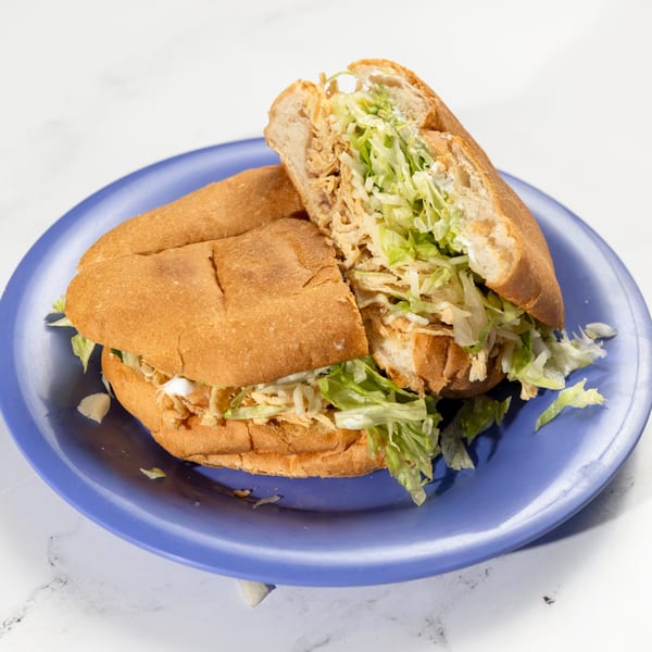 De Pasada's Mexican torta, cut in half, filled with shredded chicken and lettuce on a blue plate.