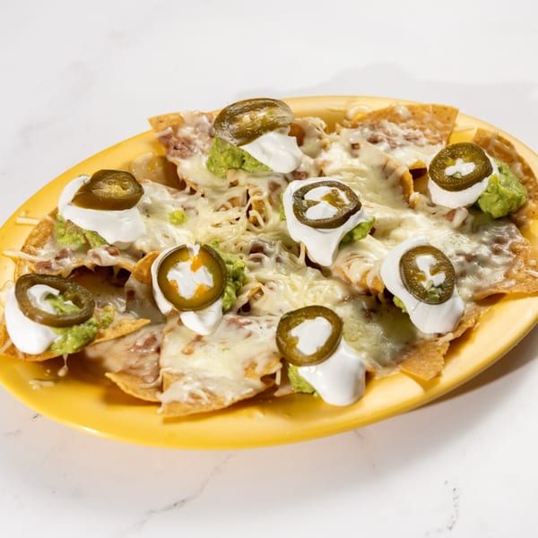 De Pasada nachos with melted cheese, guacamole, sour cream, and jalapeños on a yellow plate.