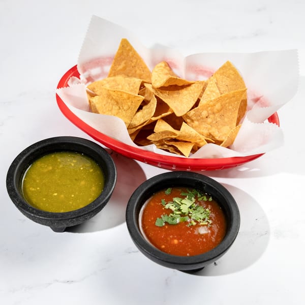 A red basket of tortilla chips with two bowls of salsa, one green and one red.